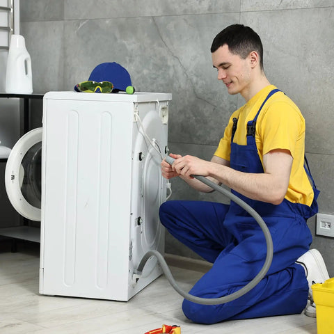 Man repairing washing machine, wearing blue overalls, handling hose