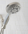 Rio Handheld Shower Head With 5 Sprays And 2.5 GPM Flow In Brushed Nickel, mounted on white tile wall