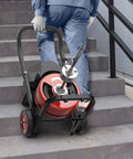 Portable Heavy Duty 75 Foot Electric Drain Auger with Auto Feed being carried up stairs for easy pipe maintenance.
