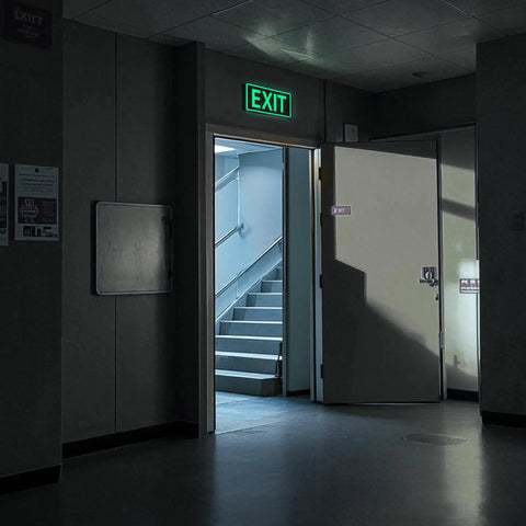 Two Pack Glow In The Dark Aluminum Exit Signs 12x7 Inches Photoluminescent Laminated For UV Weather And Fade Resistance Built Tough Easy To Spot Indoors And Outdoors For Office School Warehouse Business Fire Exit Sign on a lit hallway exit