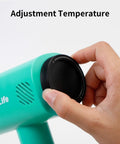 Hand adjusting temperature knob on Mint Green Heat Blower Gun With Foldable Handle For Sublimation Blanks And Shrink Wrap Film, 110V 1300W Hot Air Gun With Adjustable Dual Gear Speeds For Precise Shrink Wrapping.
