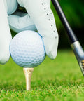 Gloved hand placing golf ball on 500 Pcs Bamboo Golf Tees 3-1/4 Inches Long Wooden Tees For Golf Practice On The Course Natural Color