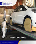 Person in protective suit preparing a white car for paint in an industrial workshop setting with masked wheels.