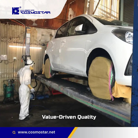 Person in protective suit preparing a white car for paint in an industrial workshop setting with masked wheels.