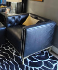 Black leather armchair with tufted backrest, gold nails, resting on a patterned carpet and surrounded by modern home decor.