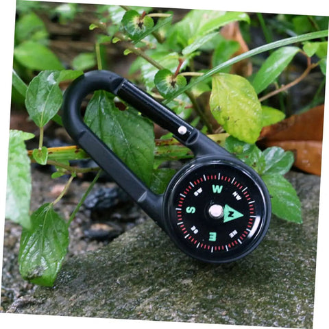 Two Pack Outdoor Hiking Compass With Carabiner Keychain in use, black, durable zinc alloy on wet stone with green foliage.