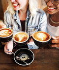 Three people holding lattes, showcasing coffee art, at a wooden table, with empty cup, related to 500 Pieces Replacement Paper Filters