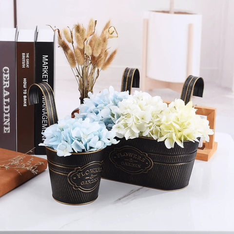 Two decorative black metal planter boxes with faux blue and white hydrangeas, labeled 'Flower Garden' on a desk.
