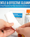 Hands using 90 Count Dry Wipes For Cleaning Bare Fiber, Connector End Faces, And Electronic Components, Lint Free Polyester Wipes In A Durable Mini Jar For Easy Debris Free Maintenance, with cleaning tools in the background.