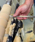 Carbide wood turning tool with 12-inch aluminum handle guiding on a wood lathe, beige turned workpiece.