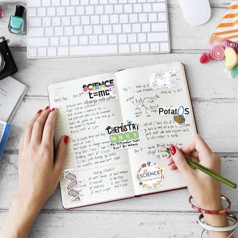 Hands writing in notebook decorated with 100 Piece Dope Science Stickers Pack Vinyl Decals For Physics Chemistry Biology Experiments