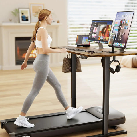 Woman using treadmill desk with dual monitors and laptops in home office setting with modern decor.