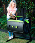 Person using the Two Stage 65 Gallon Compost Tumbler With Large Double Doors And Open Frame For Easy Unloading in a garden