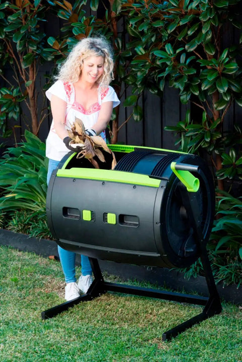 Person using the Two Stage 65 Gallon Compost Tumbler With Large Double Doors And Open Frame For Easy Unloading in a garden