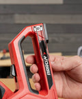 Close-up of hand holding 5-In-1 Manual Staple And Nail Gun for woodworking and craft projects in a workshop setting