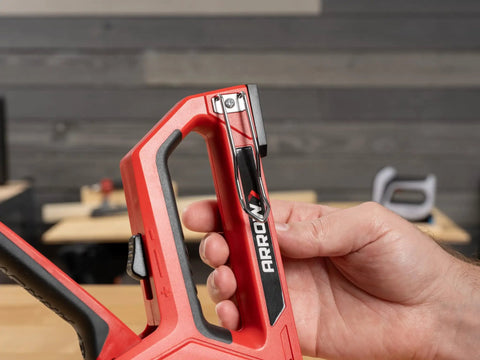 Close-up of hand holding 5-In-1 Manual Staple And Nail Gun for woodworking and craft projects in a workshop setting