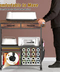 Mobile Craft Cart With 16 Vinyl Roll Holders And Built In Drawers Hooks And Shelves For Cricut Machines Heat Press And Tools All In One Rolling Workstation For Craft Room Home Or Studio Brown showing front view with wheels.