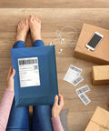 Person holding Navy Blue Poly Mailers 12x15.5 Inch 100 Pack Self Sealing Shipping Bags on wooden floor with parcels and smartphone.