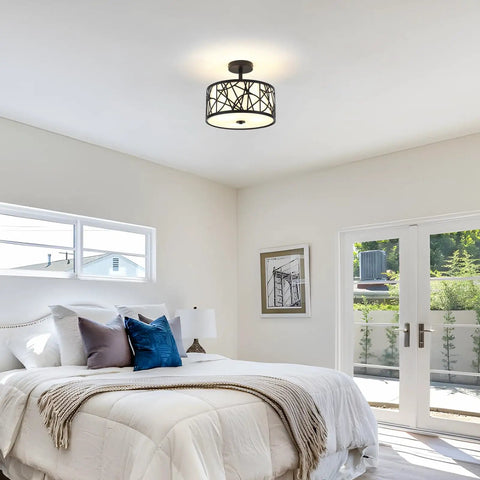 Modern bedroom with low-profile ceiling light, cozy white bedding, blue accent cushions, and bright natural light from patio doors.