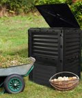 80 Gallon Large Capacity Static Compost Bin With Easy Access Hatch And Efficient Aeration System For Fast Organic Fertilizer Creation For Outdoor Use Black next to a wheelbarrow and basket outdoors