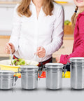 Heavy Duty Airtight Stainless Steel Coffee Canister Keeps Your Daily Grind Fresh And Locked Tight For Kitchen Storage Holds Sugar Tea And Coffee Beans In Medium Sized Jars with woman and girl cooking.