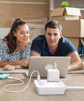 Couple using six foot power strip with three outlets and four USB ports including one USB C for cruise ship travel and home office use no surge protection ETL listed white on a wooden floor.
