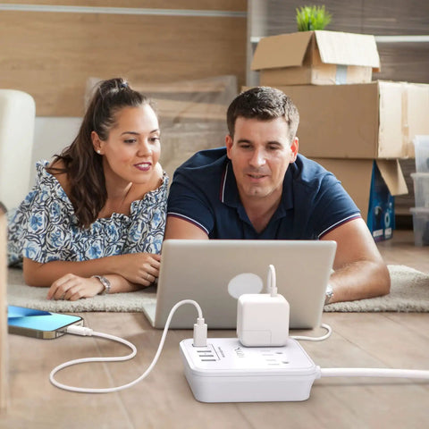 Couple using six foot power strip with three outlets and four USB ports including one USB C for cruise ship travel and home office use no surge protection ETL listed white on a wooden floor.