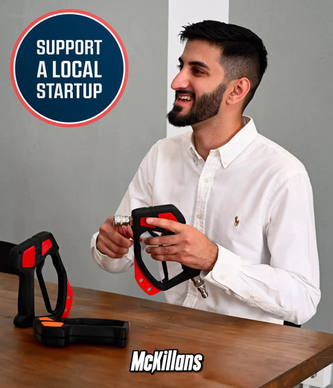 Man assembling a red and black pressure washer accessory at a table with support startup sign in background.