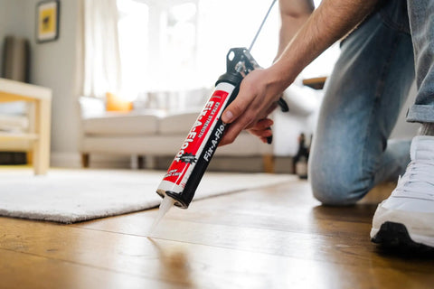 Person applying DIY Friendly Floor Repair Adhesive For Loose Tiles And Creaky Floors, Heavy Duty Strength Bond For Tile Ceramic Porcelain Marble Stone And Wood, Reattach Loose Tiles Fast Without Demolition on wooden floor with cartridge