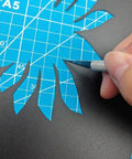 Using a carving knife from the Complete 42Pcs 3D Printer Nozzle Cleaning Tool Kit on black paper over blue cutting mat.