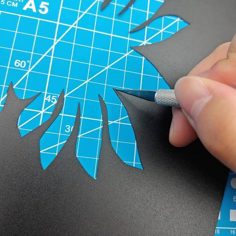 Using a carving knife from the Complete 42Pcs 3D Printer Nozzle Cleaning Tool Kit on black paper over blue cutting mat.