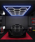 Geometric Hexagon Garage LED Light Panels With Blue Frame No-Fuss Install Ultra Bright 6500K 672W 86400LM 14 Grid Honeycomb Ceiling Lights illuminating a garage with a car.