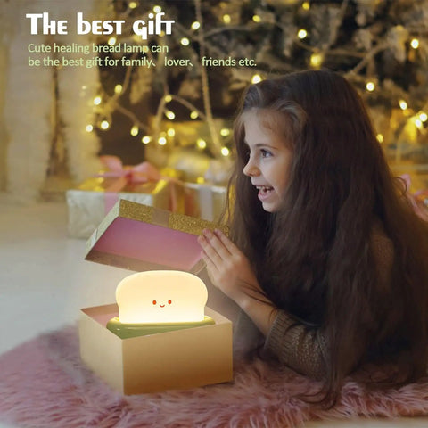 Rechargeable Cute Toaster Lamp With Smile Face, Adorable Night Light Desk Decor held by a child next to a cozy Christmas tree