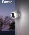 Ring Spotlight Cam Plus security camera, white, mounted on exterior wall with power cord.