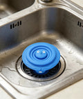 Drain Unclogger Flexible Bath Drain Cover Sealing Stopper in blue silicone on stainless steel sink, ready for use.
