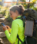 Hiker using Portable Solar Charger And Power Bank With Wireless Fast Charging, 20000mAh Battery Pack attached to backpack.