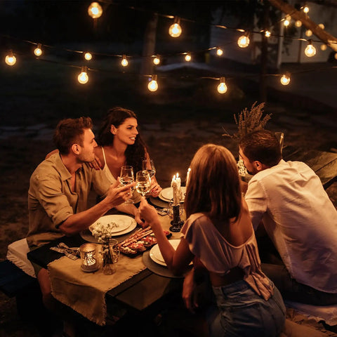Lit Outdoor Edison Style String Lights 200Ft With 102 Shatterproof ST38 LED Bulbs illuminating a cozy outdoor dining area with friends