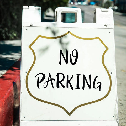 Sidewalk view of a 'No Parking' sign on a white sandwich board, demonstrating potential use for Bulk 360 Piece Self Adhesive Vinyl Letter And Number Sticker Set For Mailboxes Signs Windows Doors Cars Trucks And More 2 Inch Black Waterproof Durable Alphabet And Numerals.
