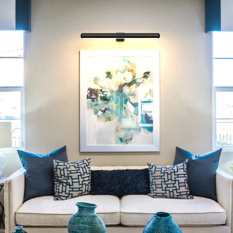 Rechargeable Magnetic LED Picture Light illuminating artwork over a modern sofa in a bright room, showcasing wall art lighting display.
