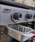 Hand removing drip tray from stainless steel grill with control knobs visible, part of Griddle Essential 5 Piece Tool Set.