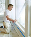 Man applying Pro Grade Masking Film Kit With Static Cling 8 Rolls Of 48 In By 180 Ft Each Keeps Film In Place indoors with hand masker tool.