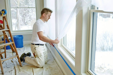 Man applying Pro Grade Masking Film Kit With Static Cling 8 Rolls Of 48 In By 180 Ft Each Keeps Film In Place indoors with hand masker tool.