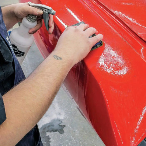 Person using Waterproof Dry And Wet Sandpaper Sheets Set 9x3.6 Inch 5 Piece Dust Free on a red surface for sanding.