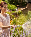 Woman using Top Tier 5 8 Inch By 75 Foot Garden Hose With Swivel Grip Connectors in a colorful garden setting.