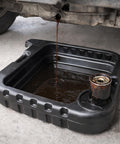 Big Fifteen Point Five Quart Oil Drain Pan With Easy Pour Spout collecting engine oil under vehicle, black.