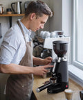 Premium 64Mm Flat Burr Coffee Grinder Featuring 100 Exact Grind Settings And Anti Static Technology For Smooth Daily Brews And Top Shelf Espresso Results In Matte Black in use with a coffee shot.