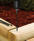Drill driving TimberLOK Heavy Duty Wood Screw 6 Inch Black into wood, showcasing corrosion resistance and tapered head in garden setting.
