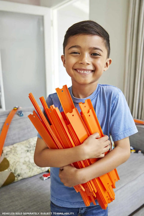 Child smiling holding orange track pieces from BHT77 Diecast Car and Track Pack in living room