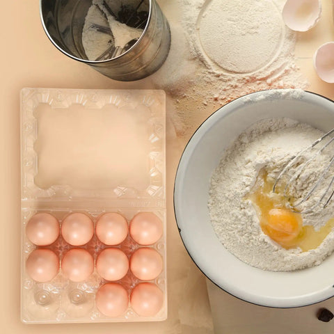 Clear Plastic Egg Cartons Bulk 200 Pack 3x4 Grid Stackable Trays For Farm Market And Home Use See Through Design Keeps Eggs Secure And Easy To See In Fridge with eggs next to a mixing bowl and flour sifter.
