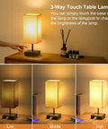 Touch Activated Bedside Lamp With USB C And USB A Charging Ports Three Way Dimmable Nightstand Light With Upgraded Fabric Shade LED Bulb Included Black Finish For Bedroom And Living Room on table showing dimming levels.